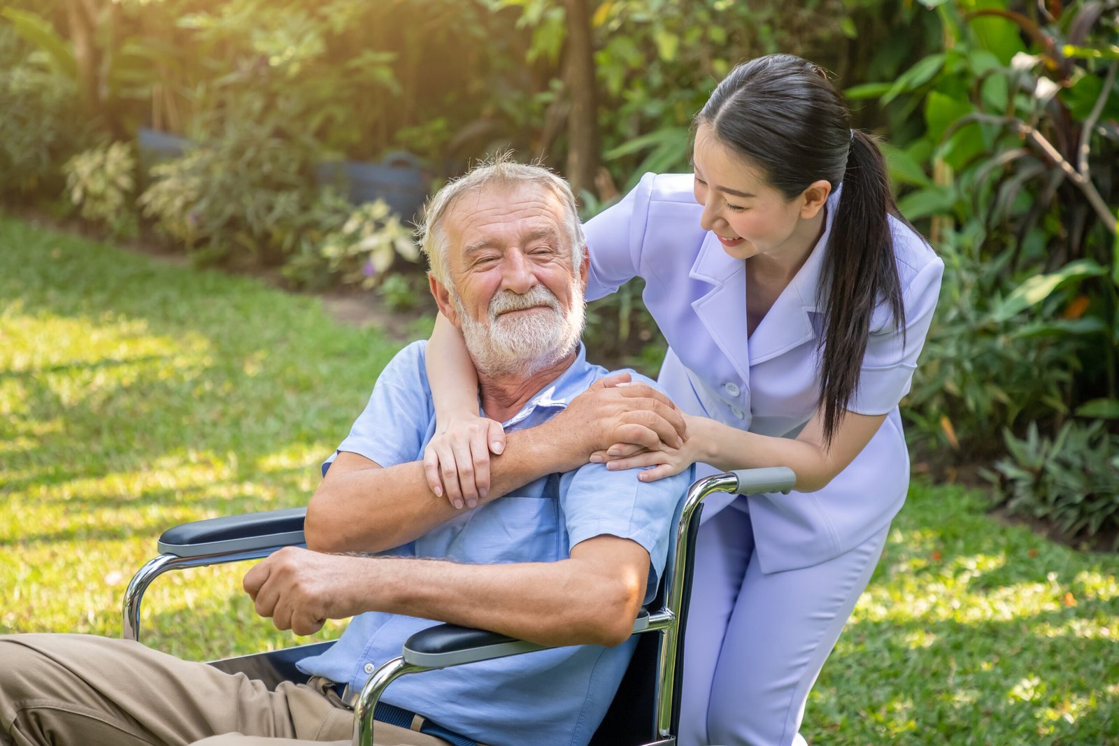Happy nurse holding elderly man hand on wheelchair in garden at